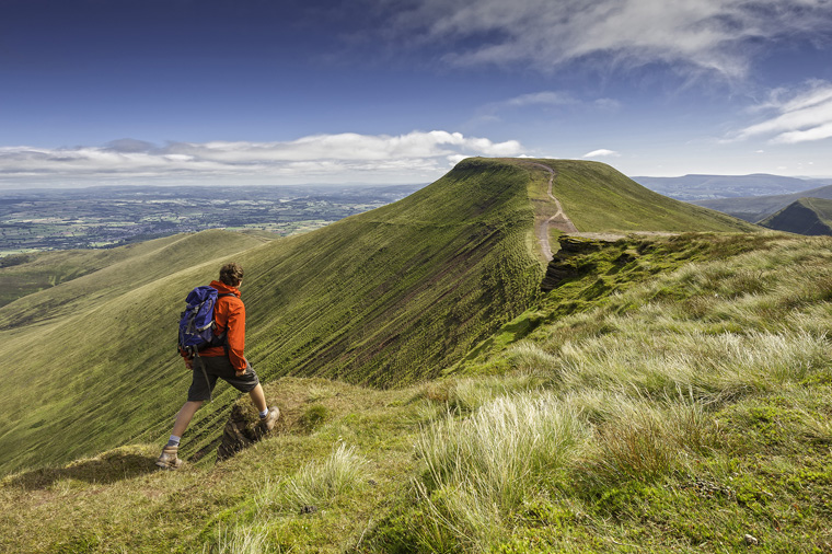 Male walker near Corn Du summit looking over to Pen y Fan Brecon Beacons | Visit Wales