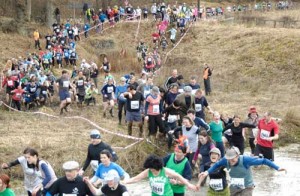 Hundreds of runners make there way though muddy rivers and banks in a long column