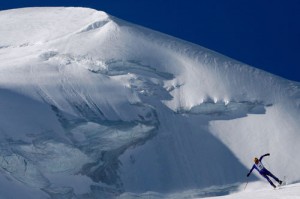 a skier races down a pristine piste with an glacial mountain backdrop and a blue sky in the background