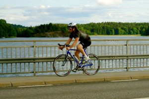 Chris Southwell on the road to becoming an Iron Man photograph of chris southwell cycling on a road with lake and trees in the background