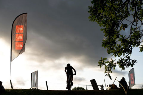 Photograph of a lone mountain biker and branding flag in the distance at the 2011 Mountain Mayhem event