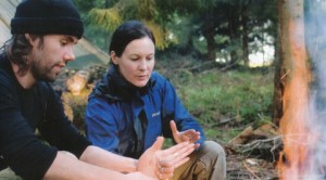 photograph of a man and woman lighting a camp fire in the woods